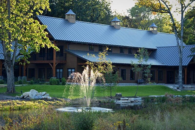 Catalpa Grove event venue seen across the ten-acre lake, its standing-seam roof and timber gables above the rain gardens