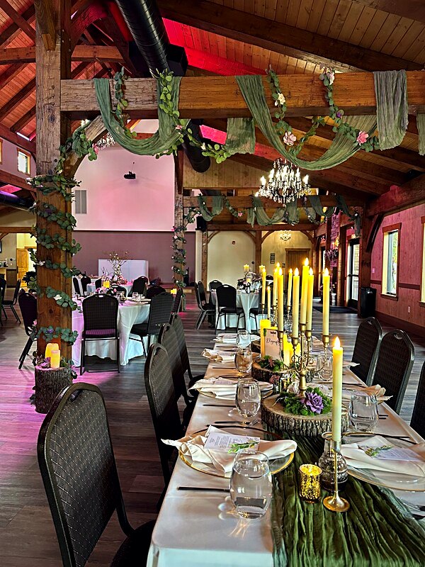 Long head table running beneath the timbers, candlelit, with greenery down the length of the cloth