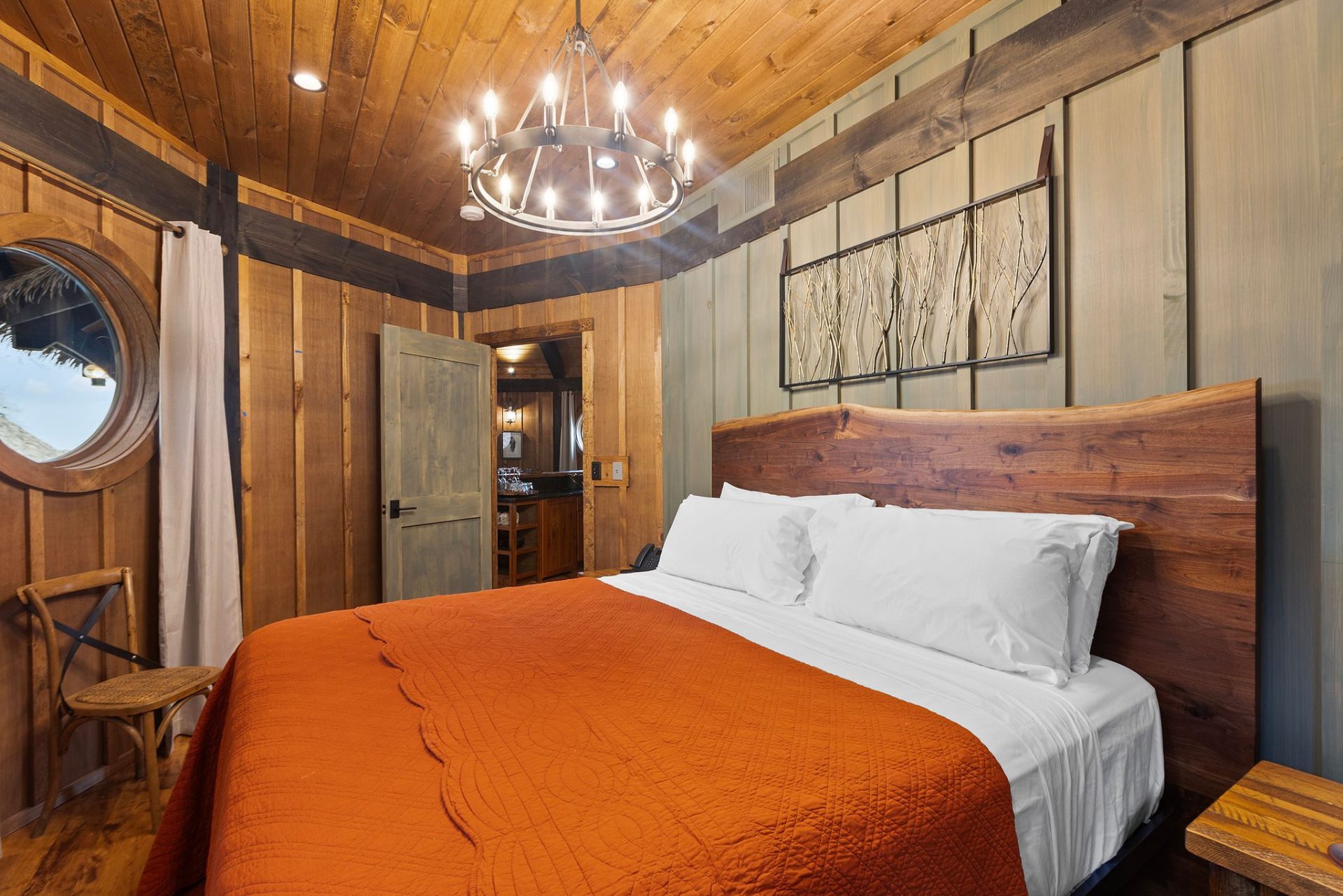 Elven Treehouse bedroom with iron chandelier, porthole window, and orange coverlet