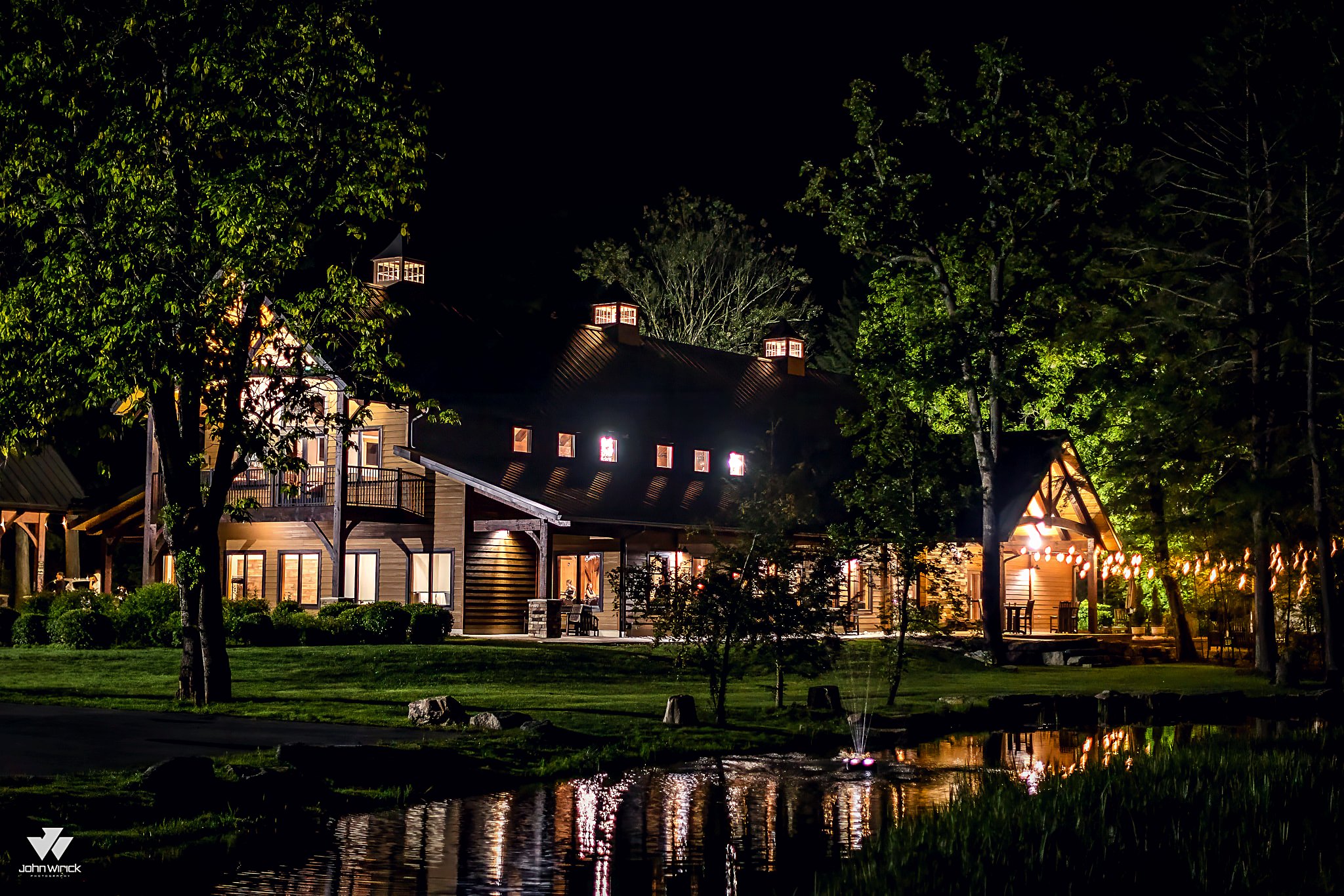 The venue at night, windows lit warm through the trees at the edge of the lawn