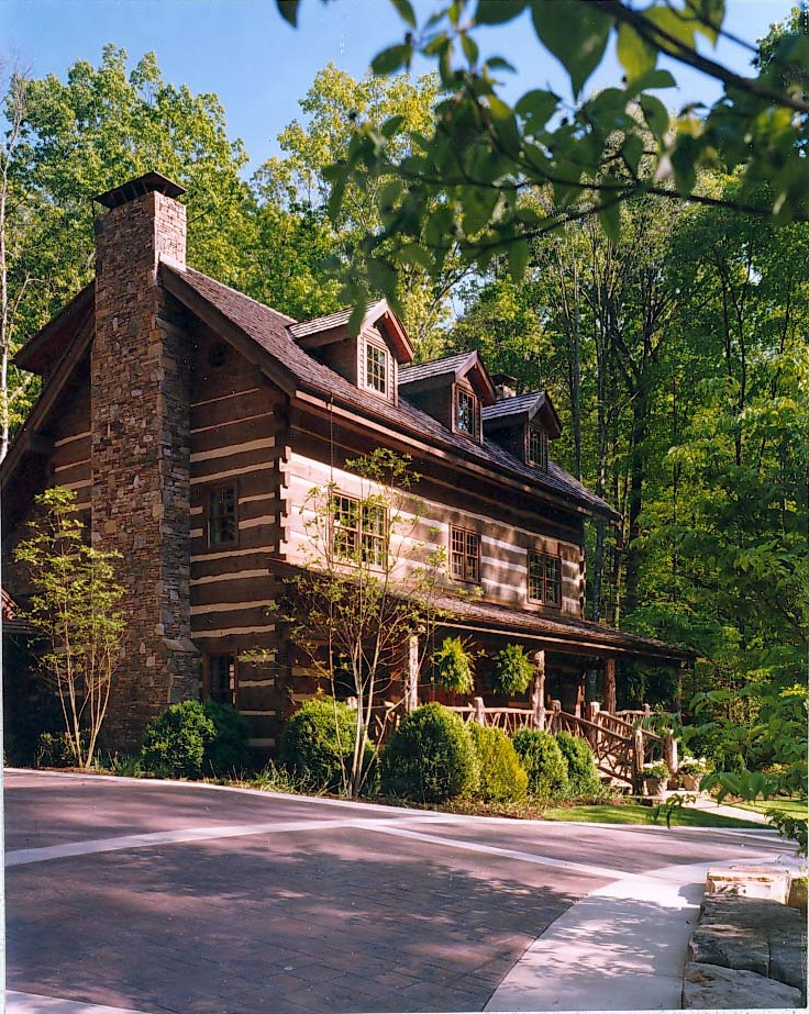 Hand-hewn log home with stone chimney under summer canopy