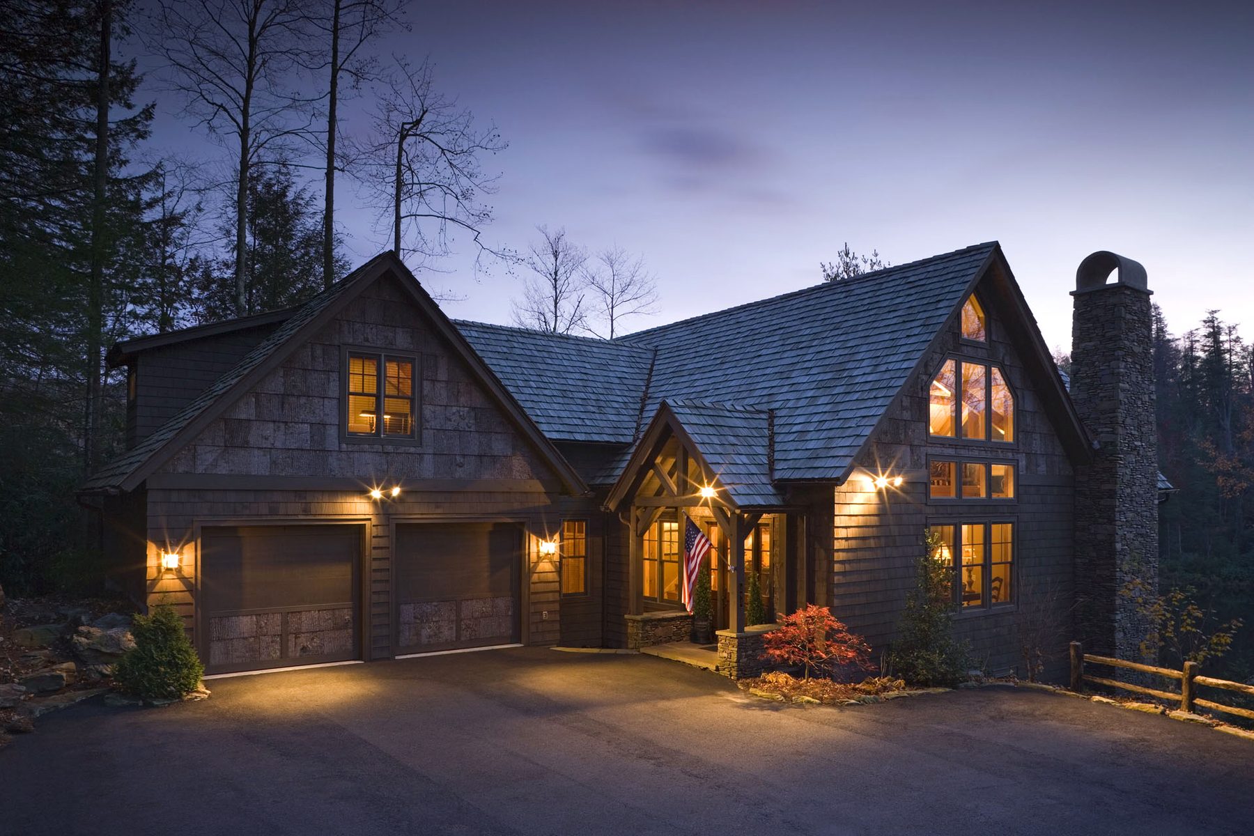 Timber frame home lit at dusk on a wooded mountain ridge