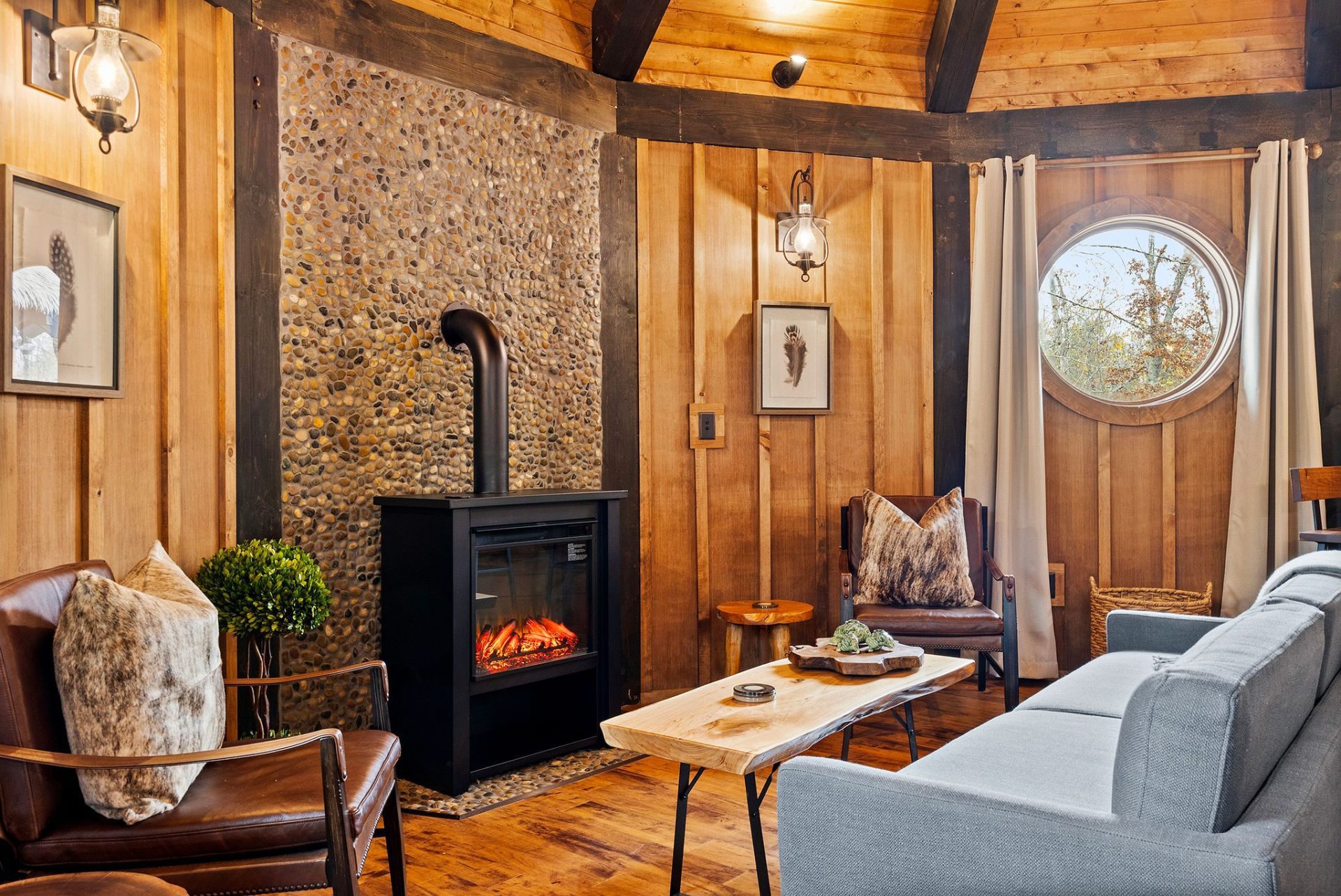 Elven Treehouse sitting area with wood stove, stone-textured wall, and porthole window