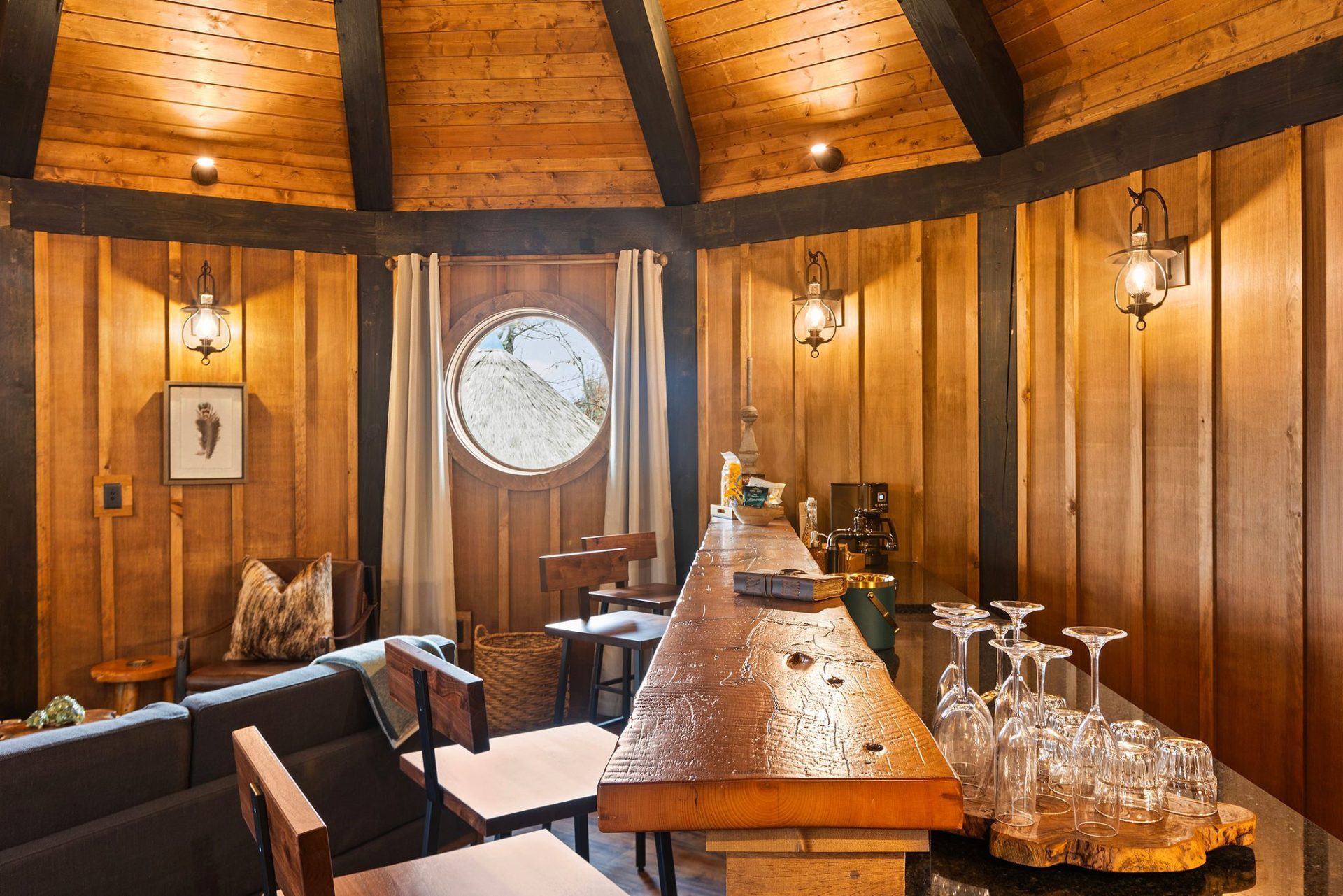 Live-edge wet bar with glassware beneath sconce-lit cedar paneling in an Elven Treehouse suite