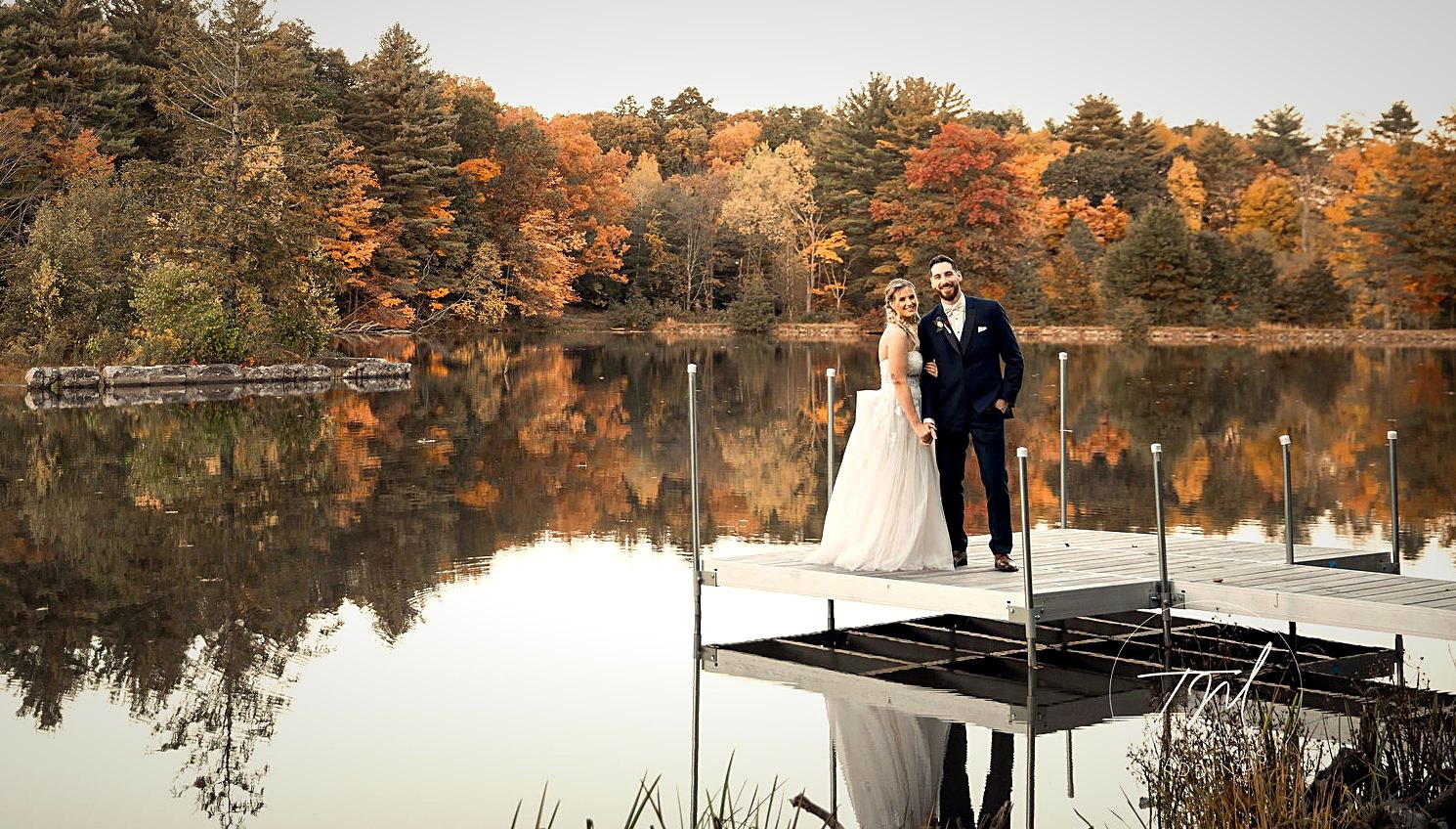 A couple on the lake dock at dusk, autumn ridge reflected in still water