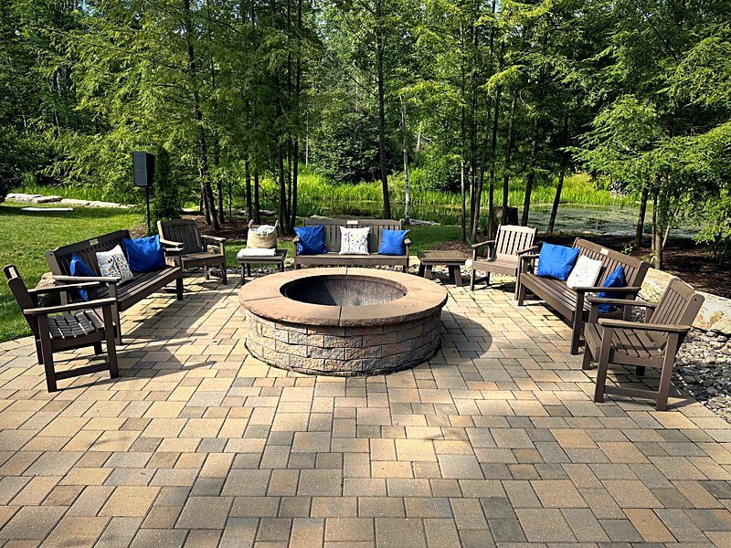 Stone fire pit ringed with Adirondack chairs on the paved outdoor gathering terrace