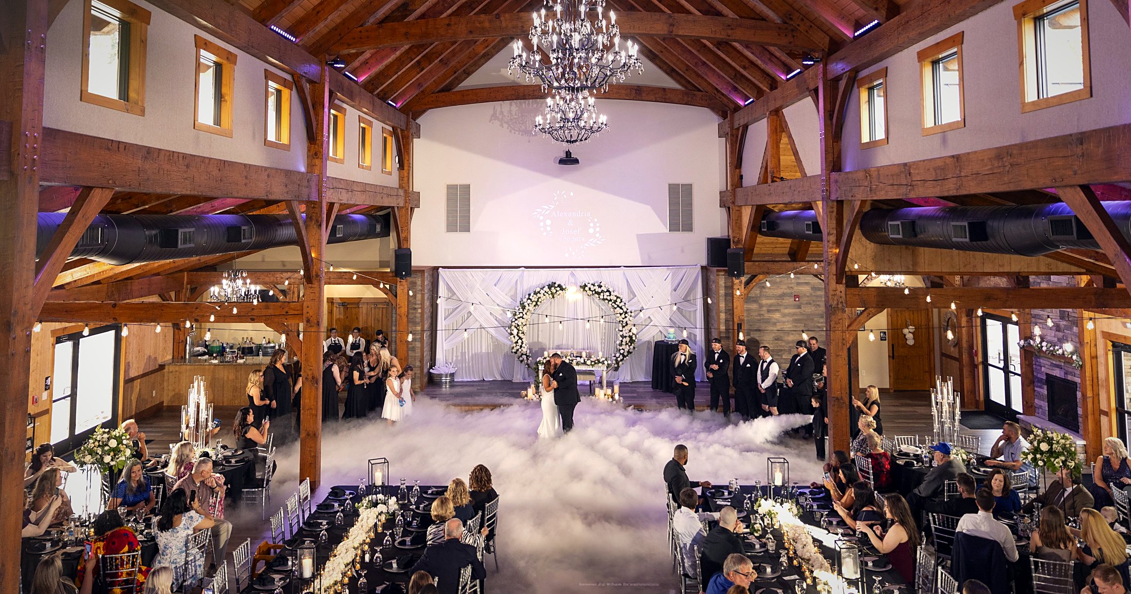 A wedding ceremony under the full span of the timber frame, guests seated to both sides