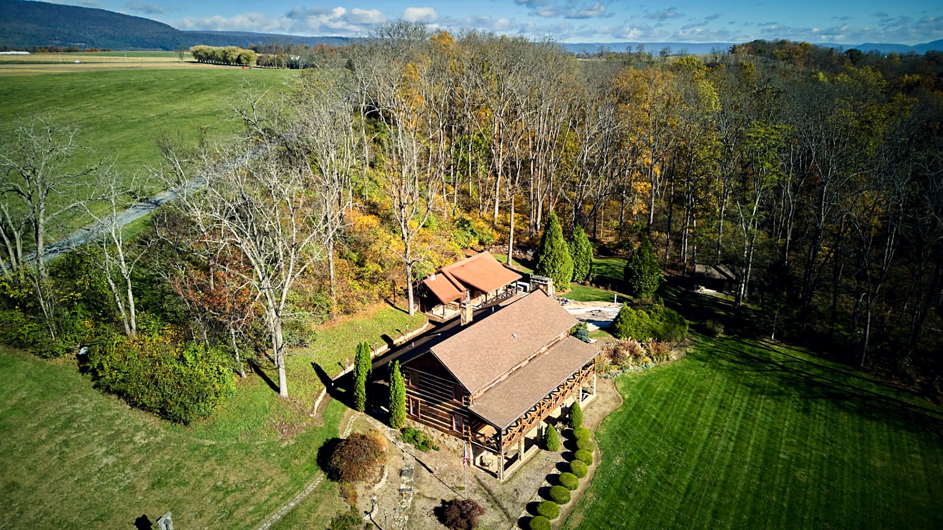 Wide aerial of the whole property — house, pool, and outbuildings against the woods