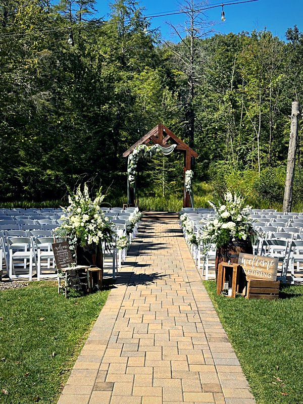 Outdoor ceremony aisle in paver stone leading to a timber arbor, white chairs set on the lawn