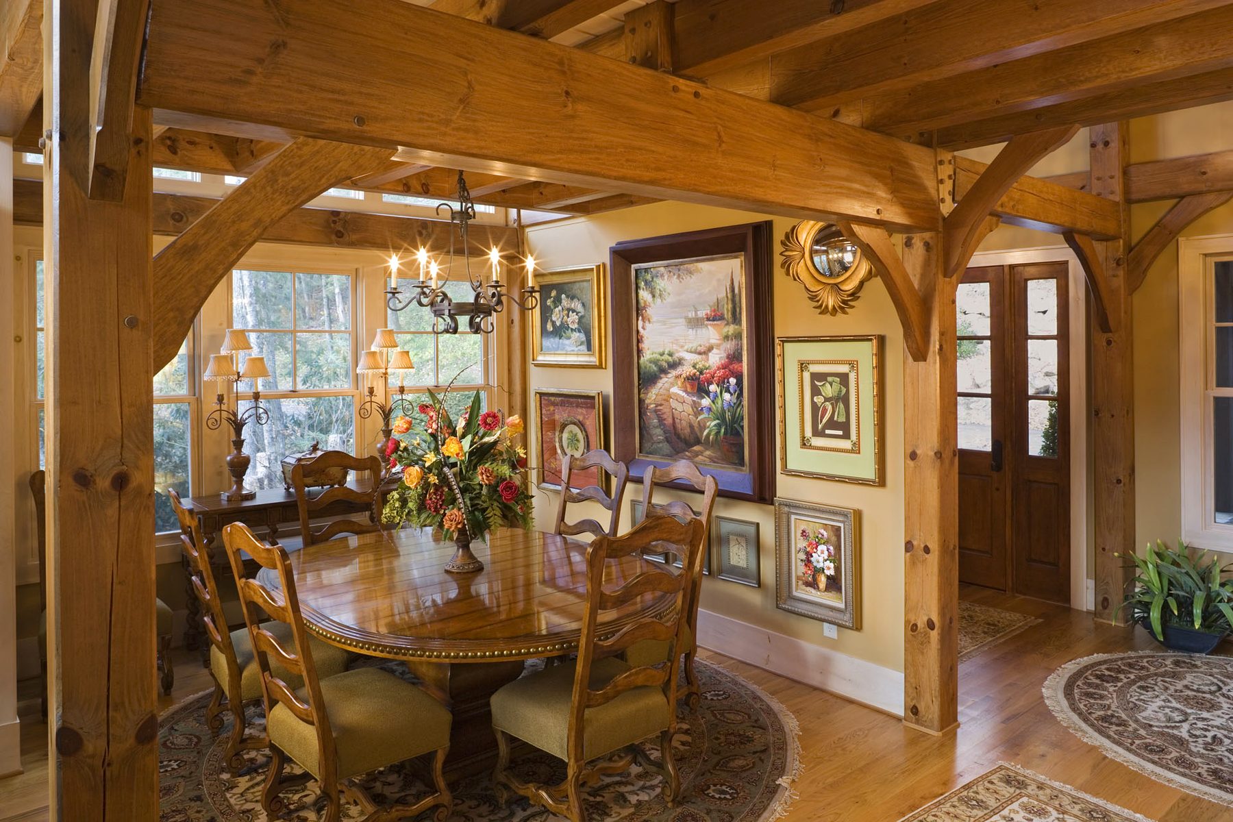 Dining room under exposed timber framing with chandelier and lake windows