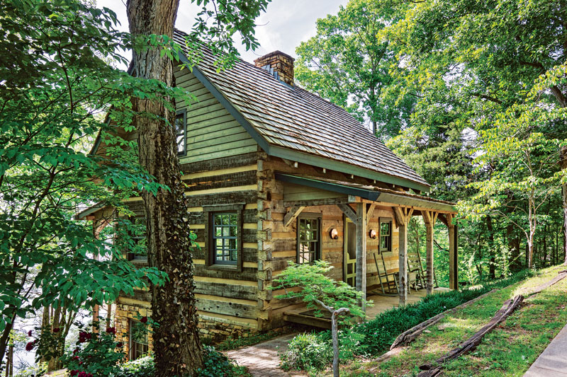 Hand-hewn log cabin with cedar shake roof and covered porch in a wooded hillside