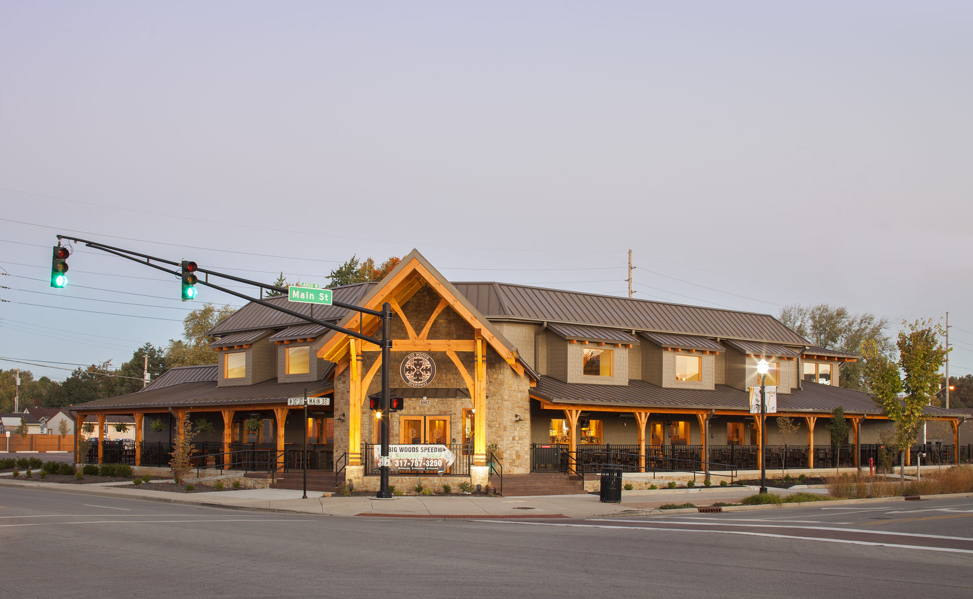 Big Woods Speedway exterior at dusk — heavy timber porch and gabled entry on Main Street, Speedway, Indiana