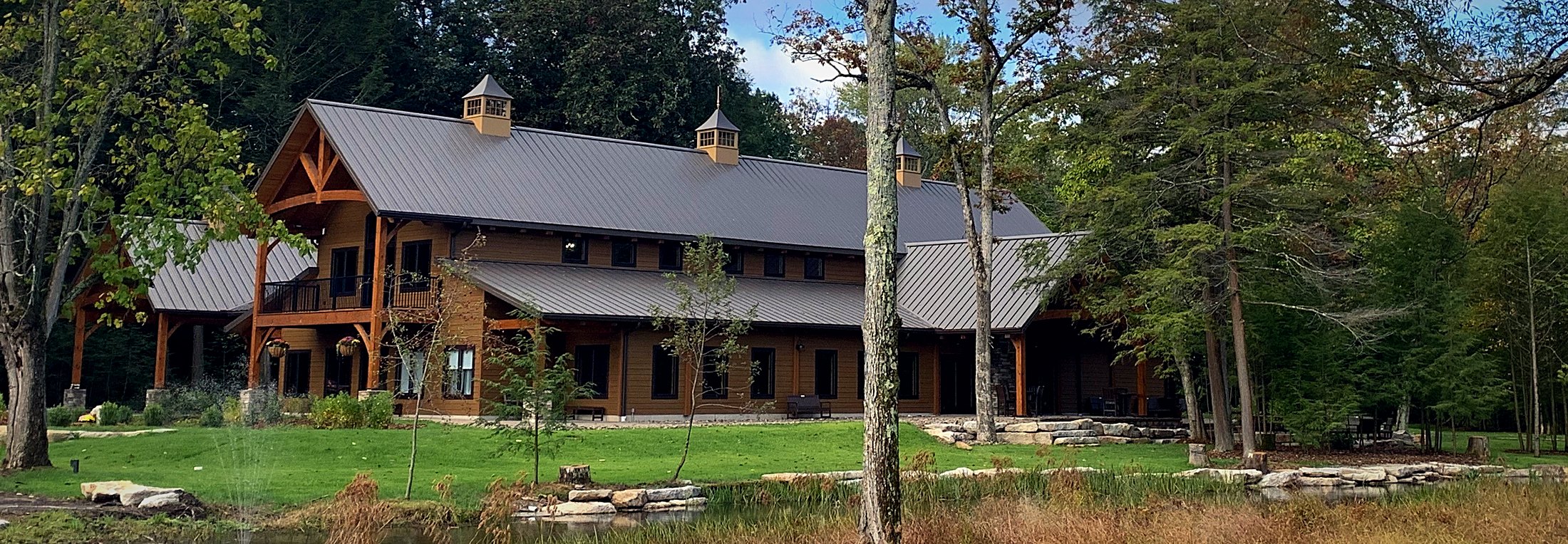 Long exterior elevation across the mown lawn, standing-seam roof running the length of the hall