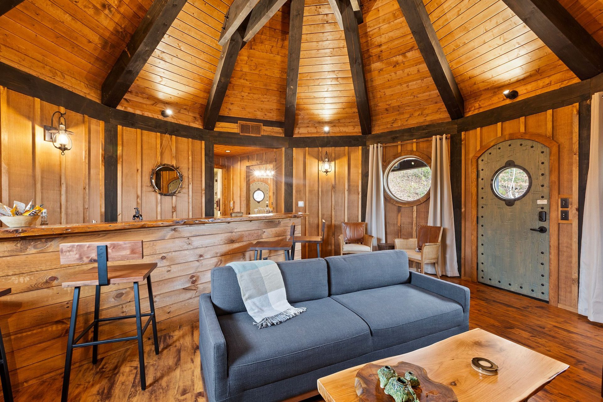 Elven Treehouse living room under a radial timber-rafter dome with round windows and an arched plank door