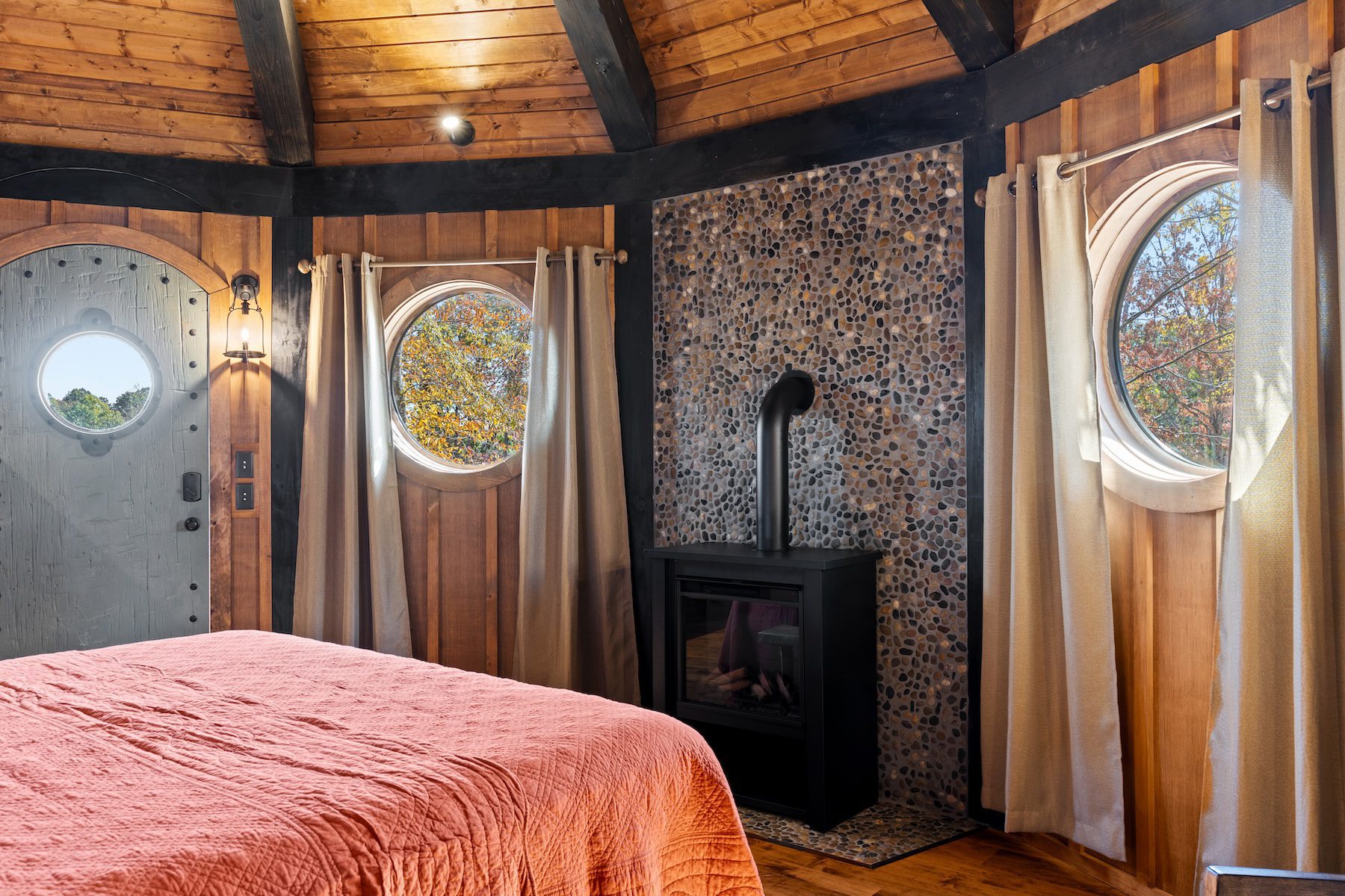 Cozy wooden Elven Treehouse suite with round windows, fireplace, and red quilt