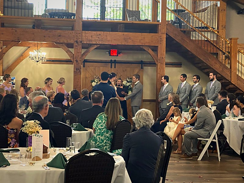 Ceremony held indoors under the timber frame with guests seated on both sides of the aisle