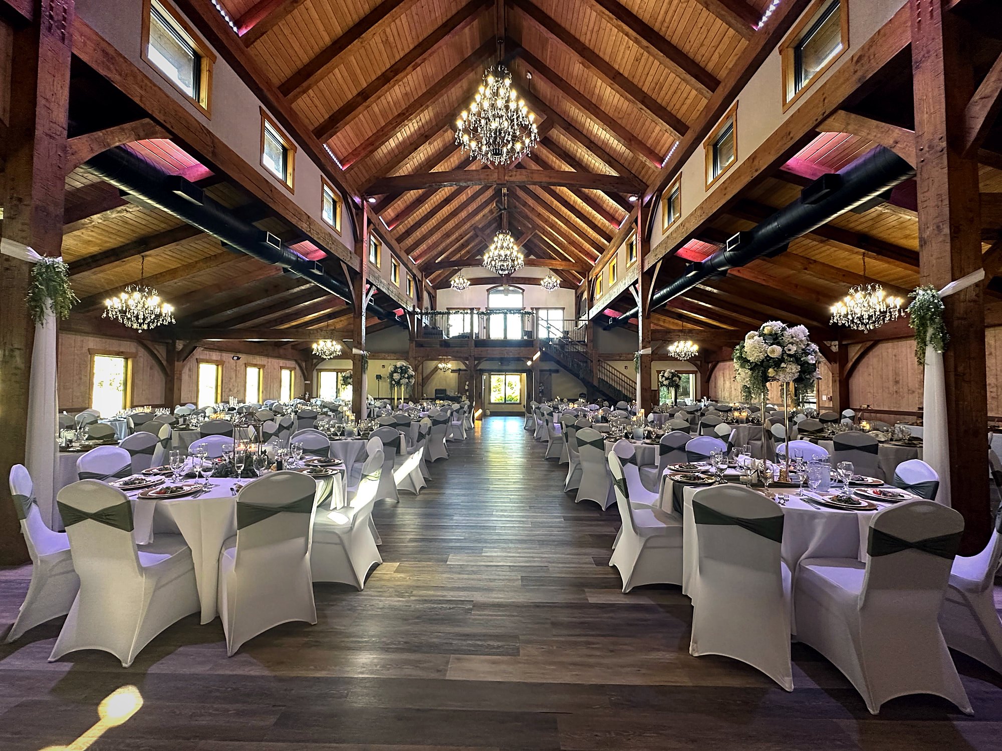The timber hall lit violet at the truss line, chairs dressed in white for a reception