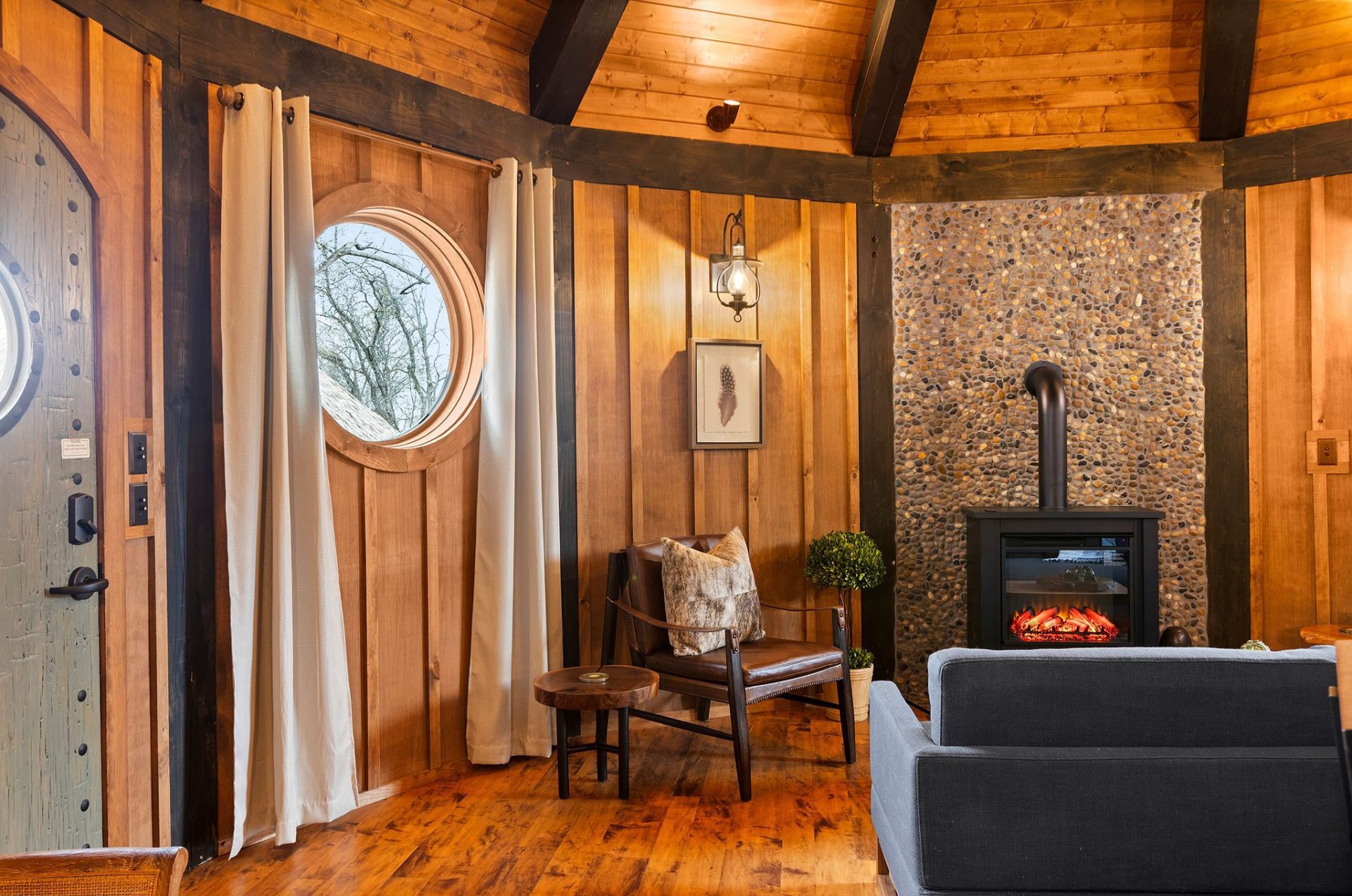 Elven Treehouse entry with studded arched door, curtained round window, and wood stove