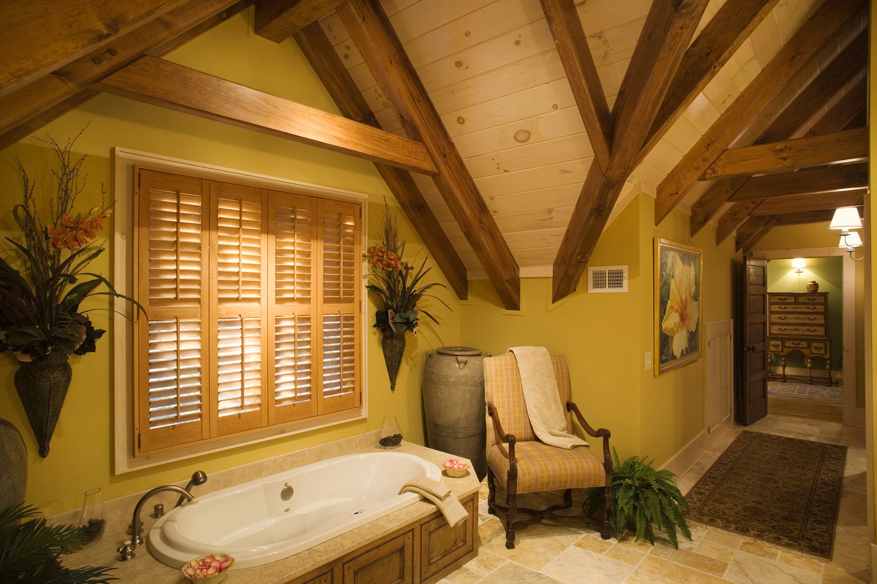 Master bath with soaking tub set beneath timber rafters and plantation shutters