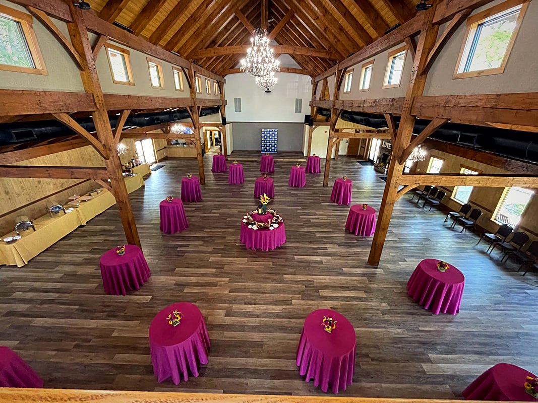 Reception tables in deep rose linen beneath the timber frame and chandeliers