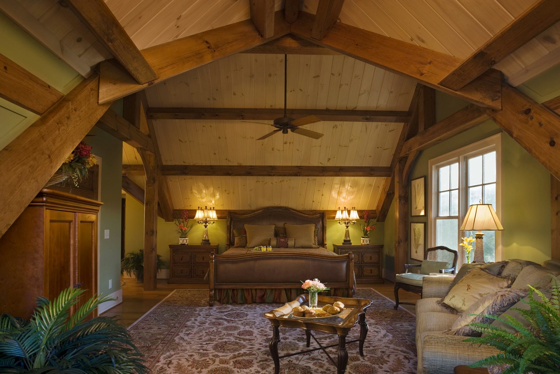 Master suite beneath timber trusses with a sitting area and windows to the treeline